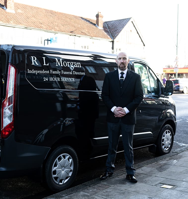 black and white photo of  hearse and man next to it